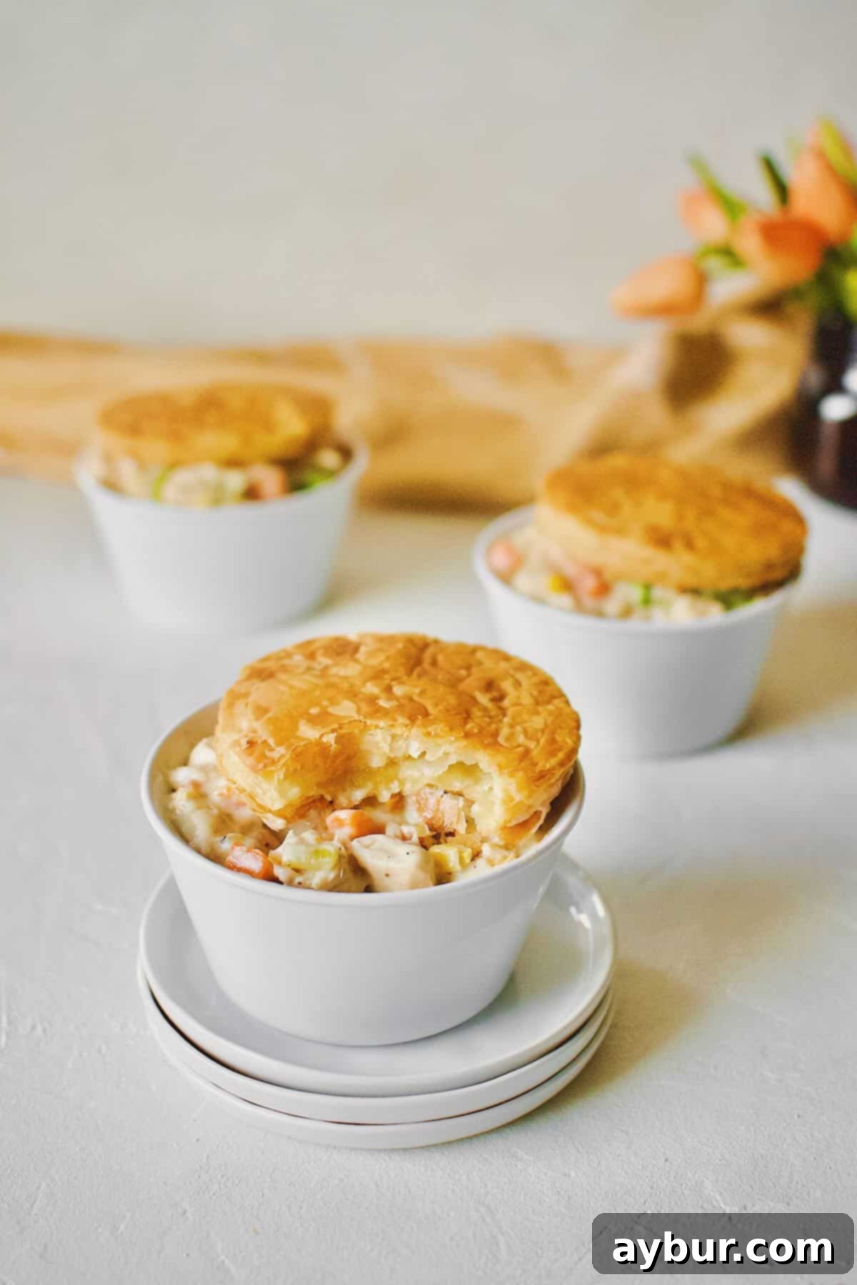 3 individual Chicken Pot Pie with Puff Pastry tops. One with a bite taken out of it.