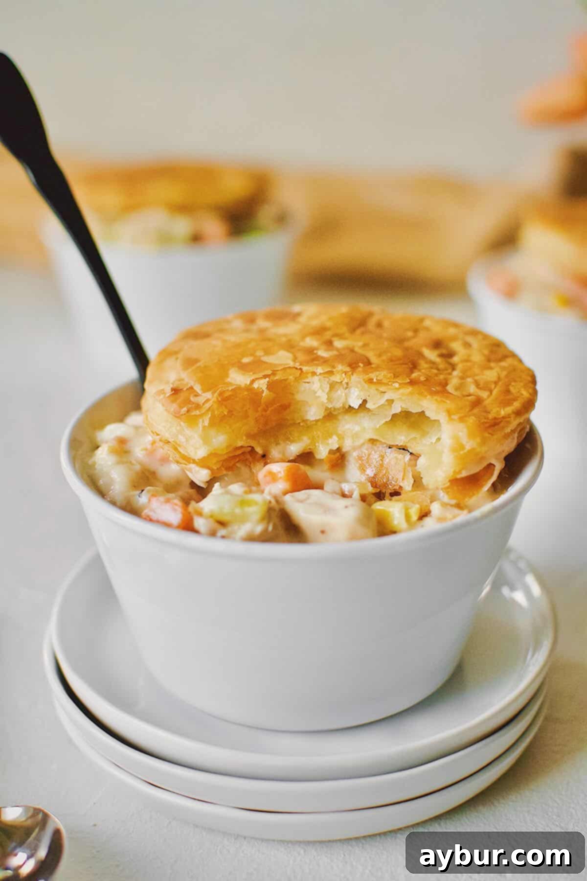 3 individual Chicken Pot Pie with Puff Pastry tops. One with a bite taken out of it.