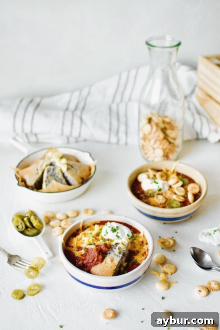 Two bowls of Spicy Texas Chili, richly colored, surrounded by a variety of fresh toppings like shredded cheese, green onions, and jalapeño slices.