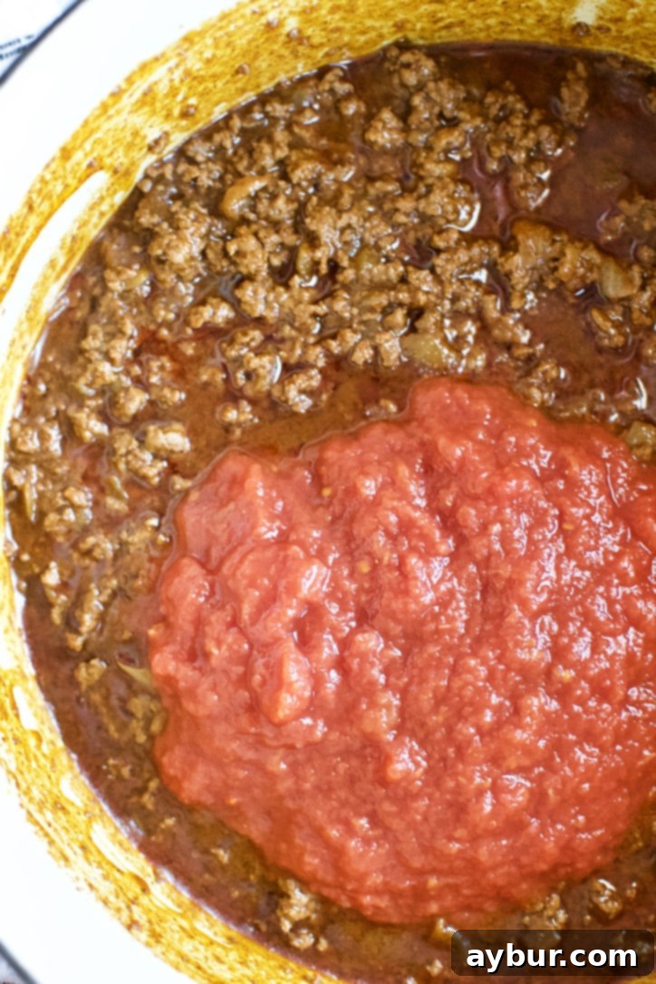 Cans of crushed tomatoes being added to the simmering chili pot to complete the base.