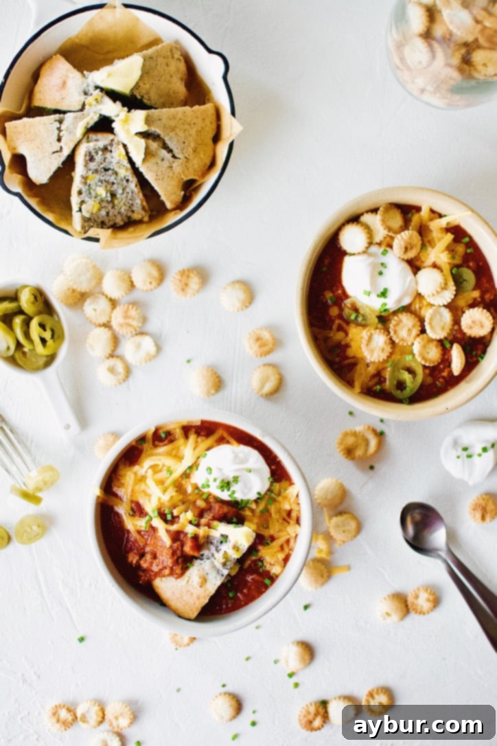 A vibrant table setting featuring two bowls of Spicy Texas Chili with an array of toppings including cheese, sour cream, and fresh herbs, inviting guests to customize their meal.