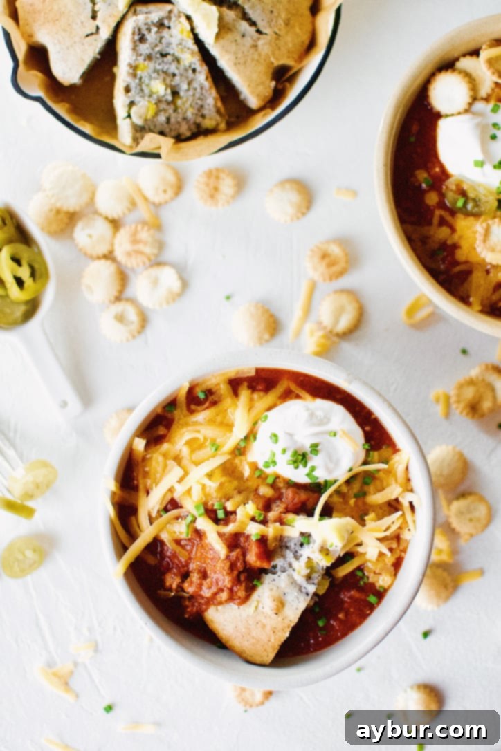 Overhead shot of two steaming bowls of Spicy Texas Chili garnished with cheese and sour cream, against a rustic wooden background.