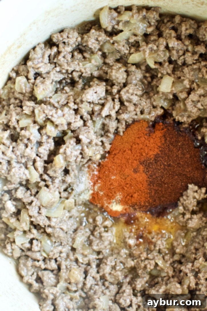A generous amount of chili spices being added to the browned ground beef and onion mixture in a pot.