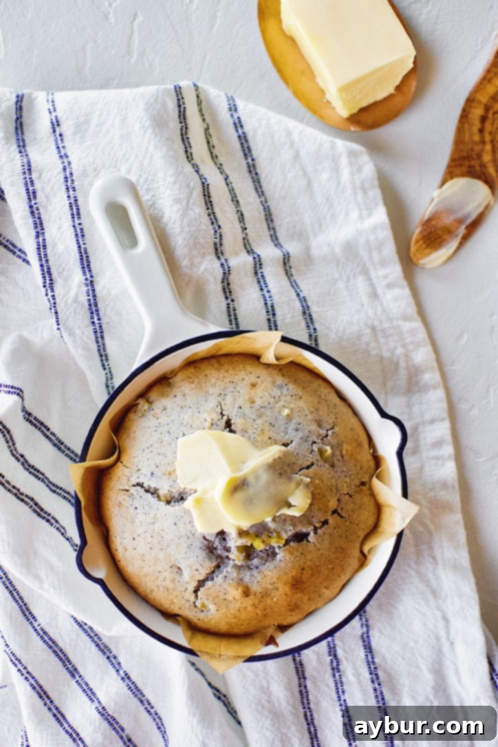 A warm, baked blue cornbread in a skillet, generously spread with a thick layer of melting butter, ready to be enjoyed.