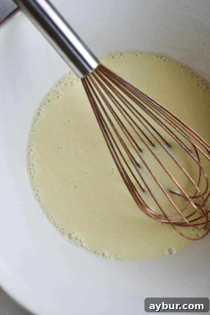 The same bowl with milk, oil, and eggs, now thoroughly whisked until lightly frothy.