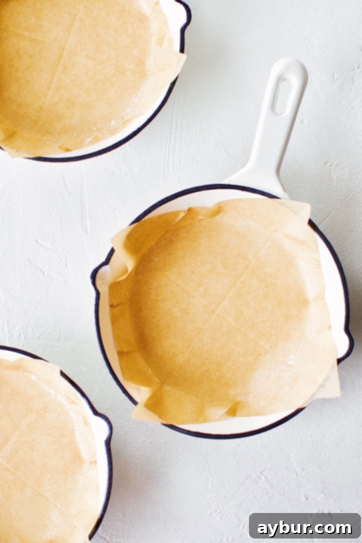 A mini cast-iron skillet meticulously lined with parchment paper and lightly sprayed, prepared for the cornbread batter.