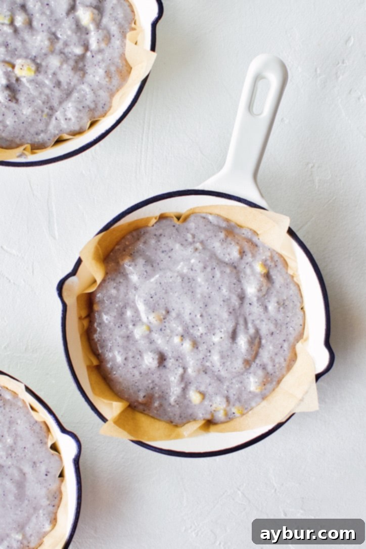 Blue cornbread batter carefully spooned into a prepared mini cast-iron skillet, ready for baking.