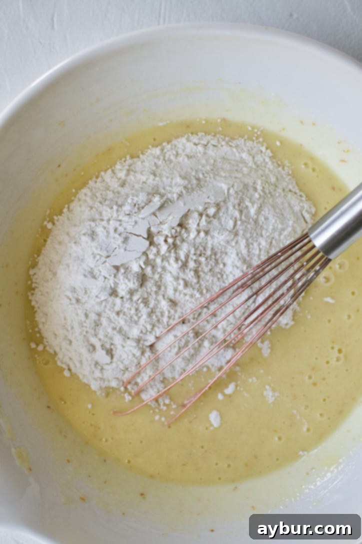 Adding the flour to the blended the wet ingredients with the sugar in a bowl.