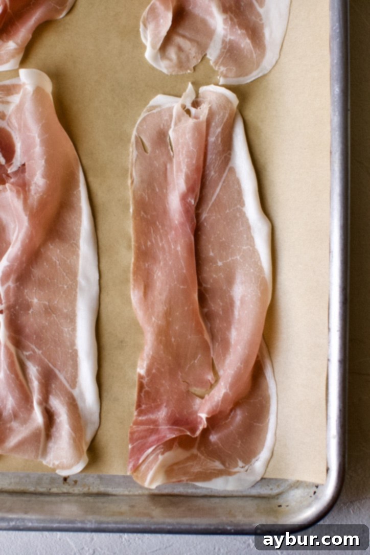 Prosciutto slices arranged on a parchment-lined baking sheet.