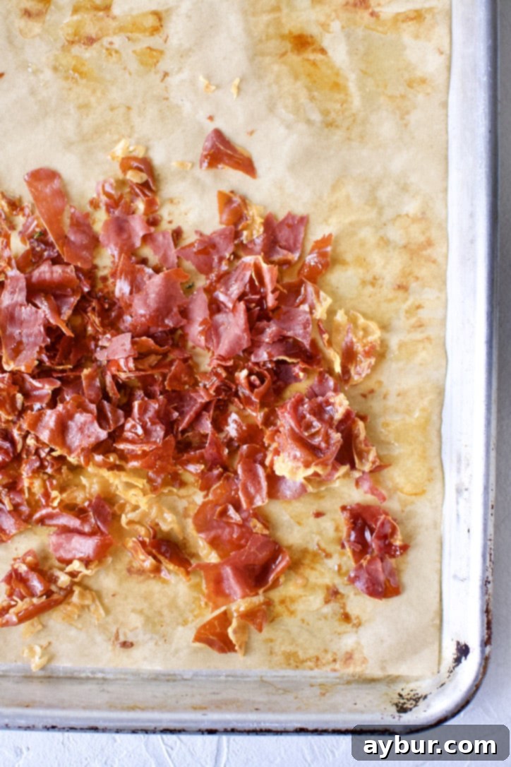 More crispy prosciutto on a baking sheet, ready to be crumbled.