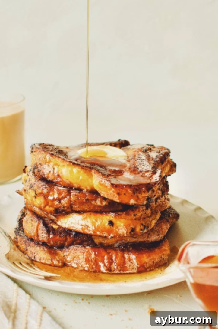A stack of perfectly cooked Custard French Toast slices, caramelized with cinnamon sugar, topped with a dollop of butter and a drizzle of maple syrup, invitingly presented.