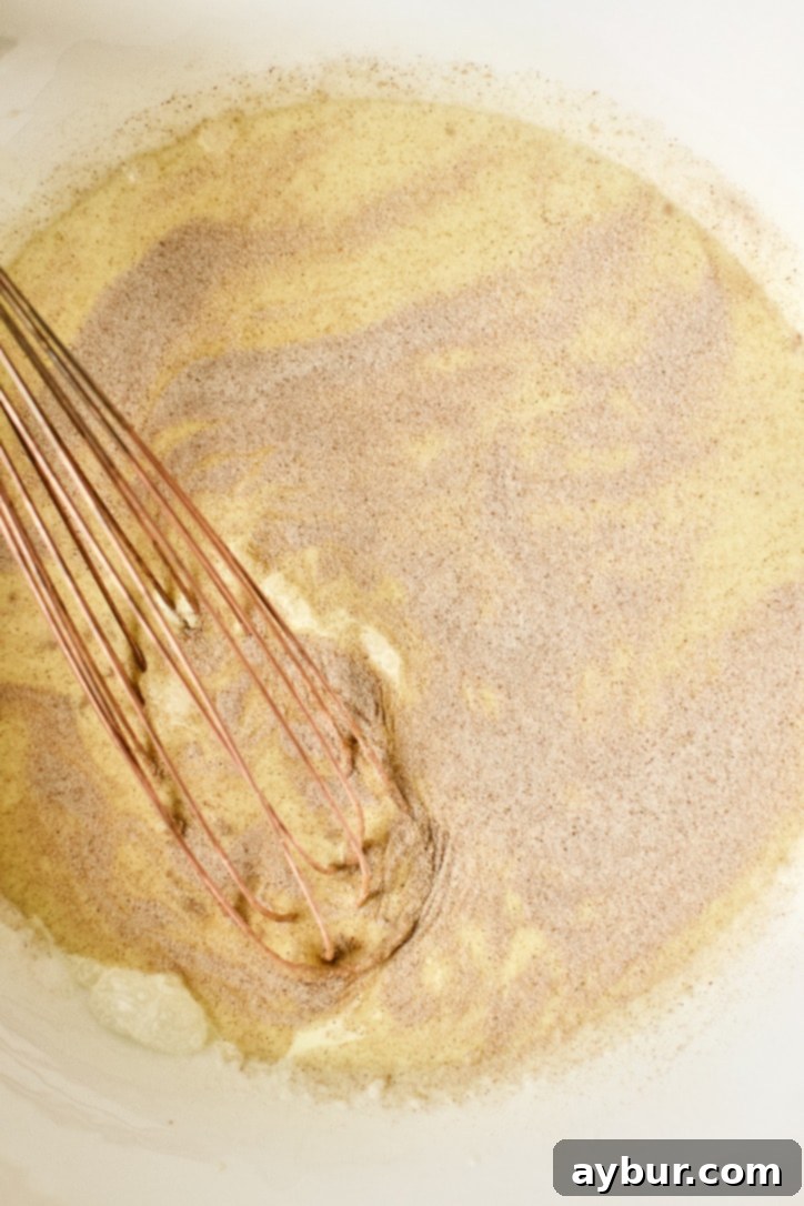 Detailed shot of whisking egg yolks, heavy cream, half and half, and vanilla extract with cinnamon sugar in a bowl, creating the French toast custard base.