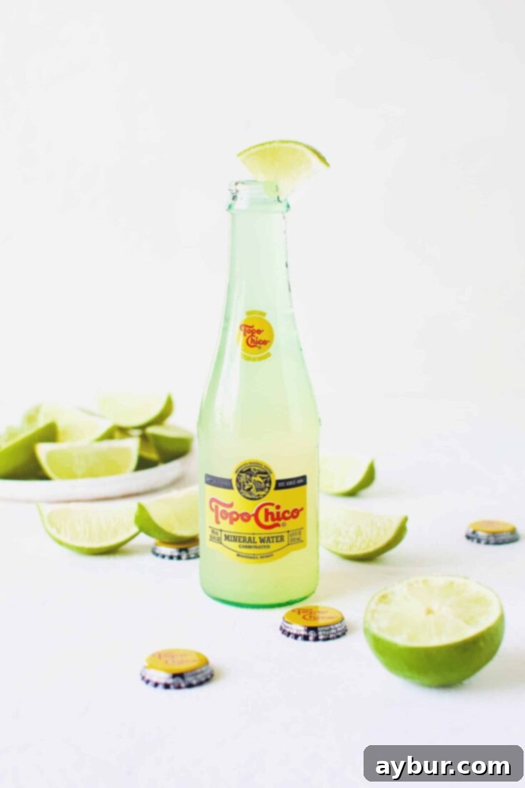 A refreshing Topo Chico Margarita served directly in the iconic glass bottle, garnished with fresh lime wedges, sitting on a rustic surface.