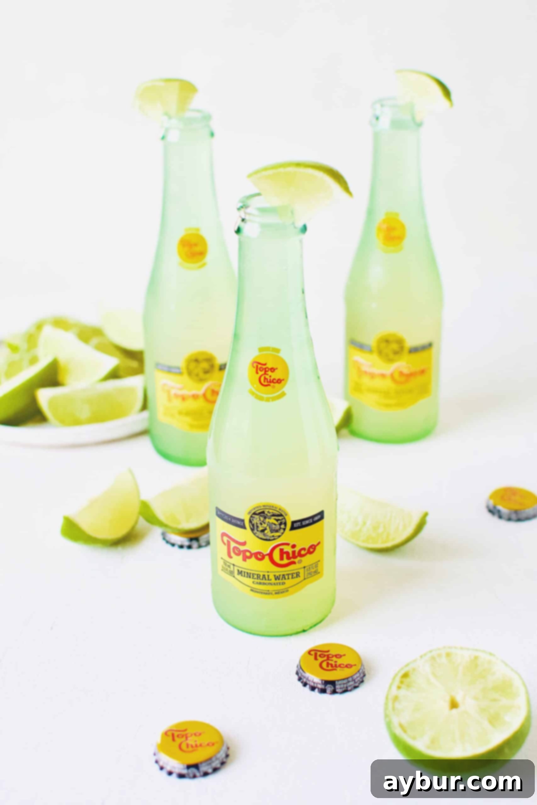 Three Topo Chico Margaritas, expertly mixed and ready to serve, each garnished with a fresh lime wedge and sitting beside whole and sliced limes.