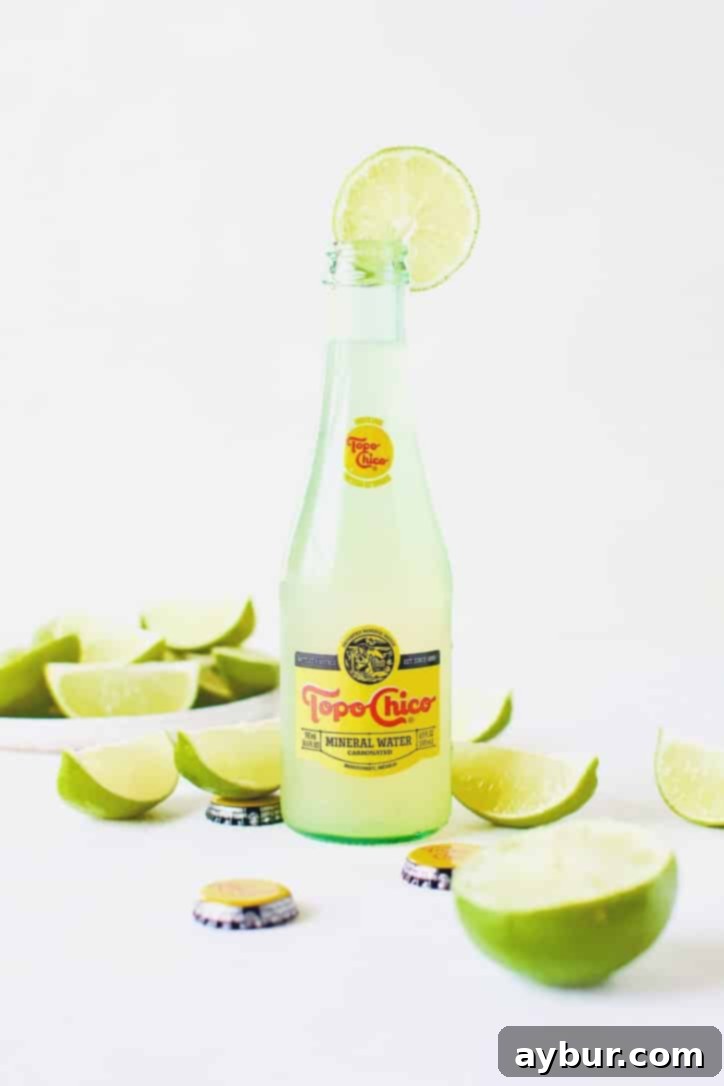 Topo Chico Sparkling Margarita 5 Multiple Topo Chico Margaritas in bottles, garnished with lime, against a rustic background.