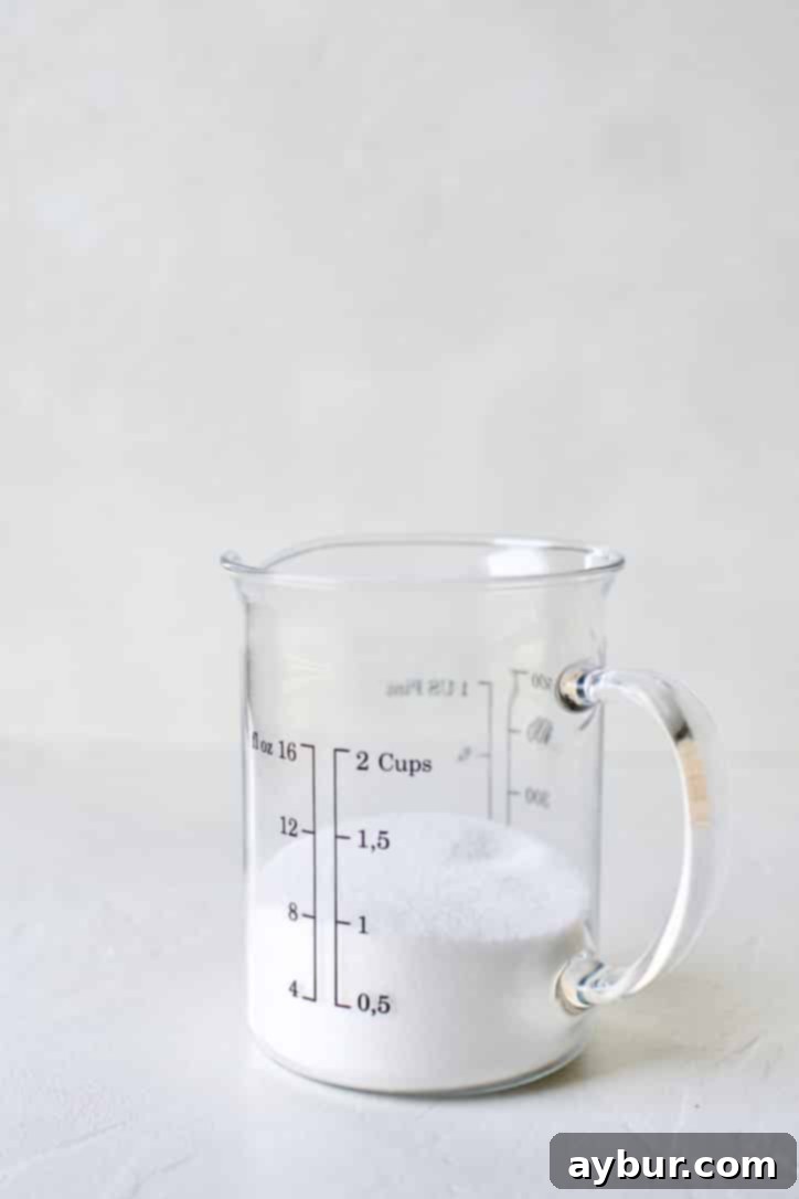 A measuring cup containing one cup of granulated sugar, ready for making simple syrup.