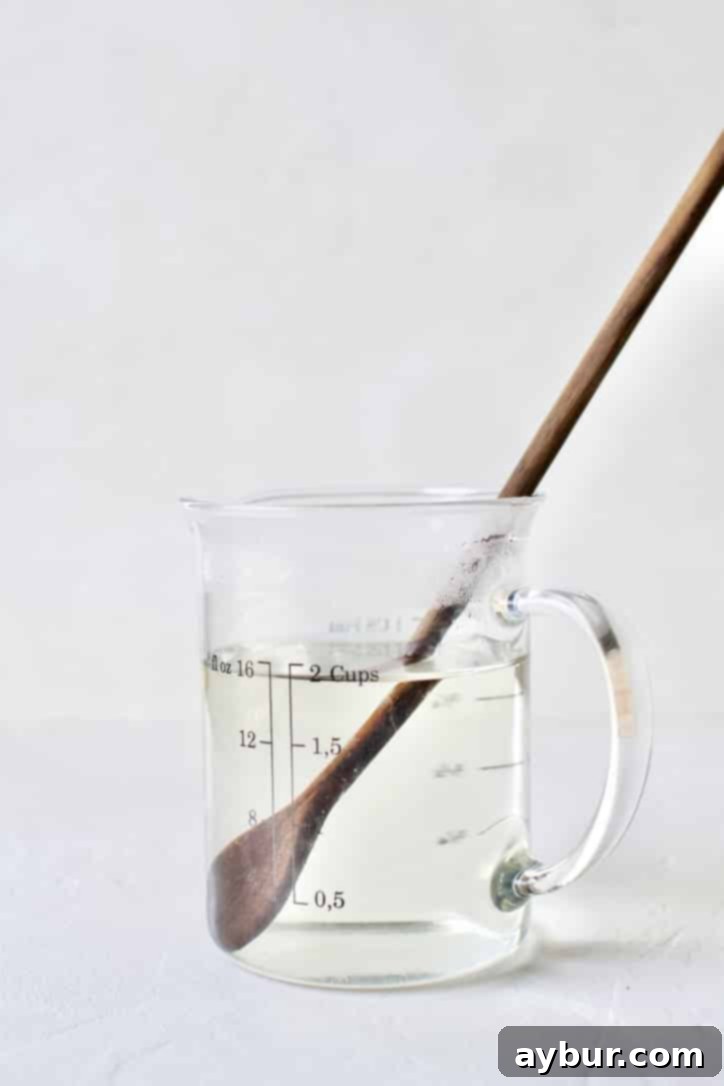 Boiling water being poured over sugar in a measuring cup, then stirred until dissolved to create homemade simple syrup.