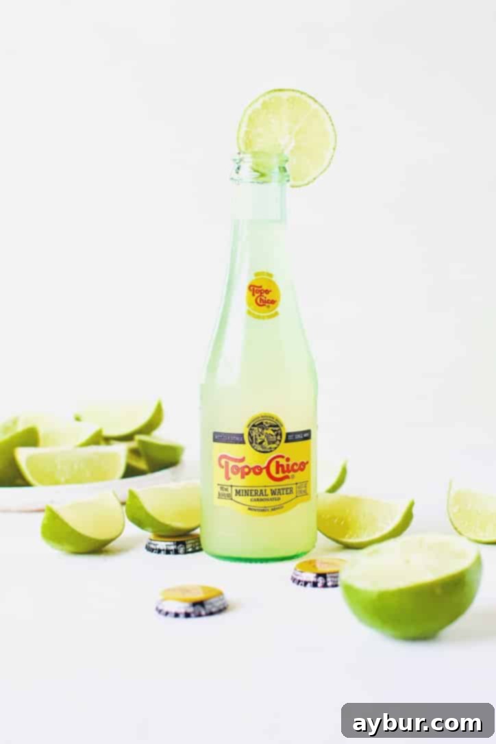 Topo Chico Sparkling Margarita 9 A selection of Topo Chico Margaritas, some in bottles, some in glasses, all garnished with lime wedges, on a rustic surface.