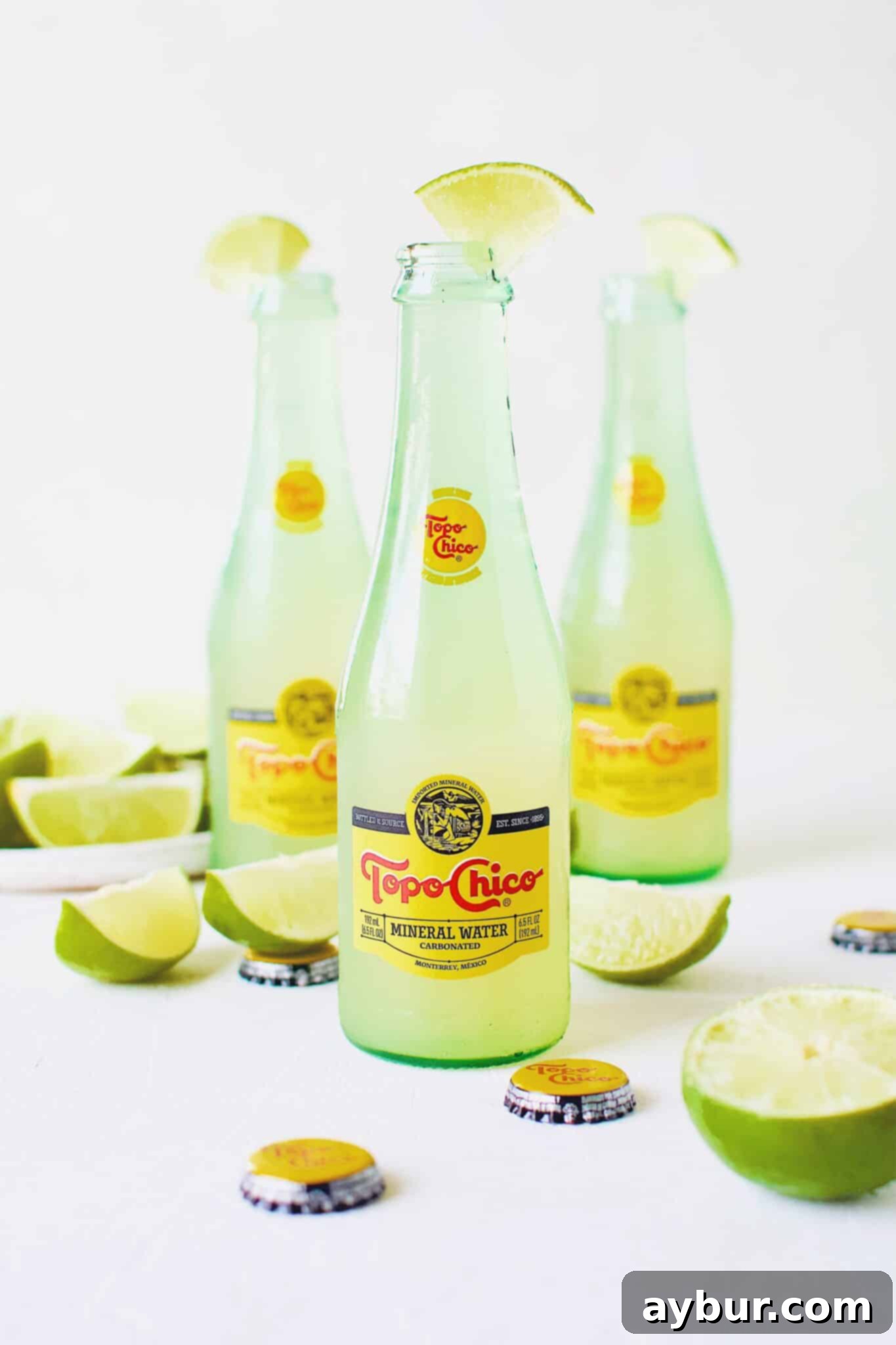 Topo Chico Sparkling Margarita 10 A beautifully presented Topo Chico Margarita in a bottle, surrounded by lime slices, gleaming in the light.