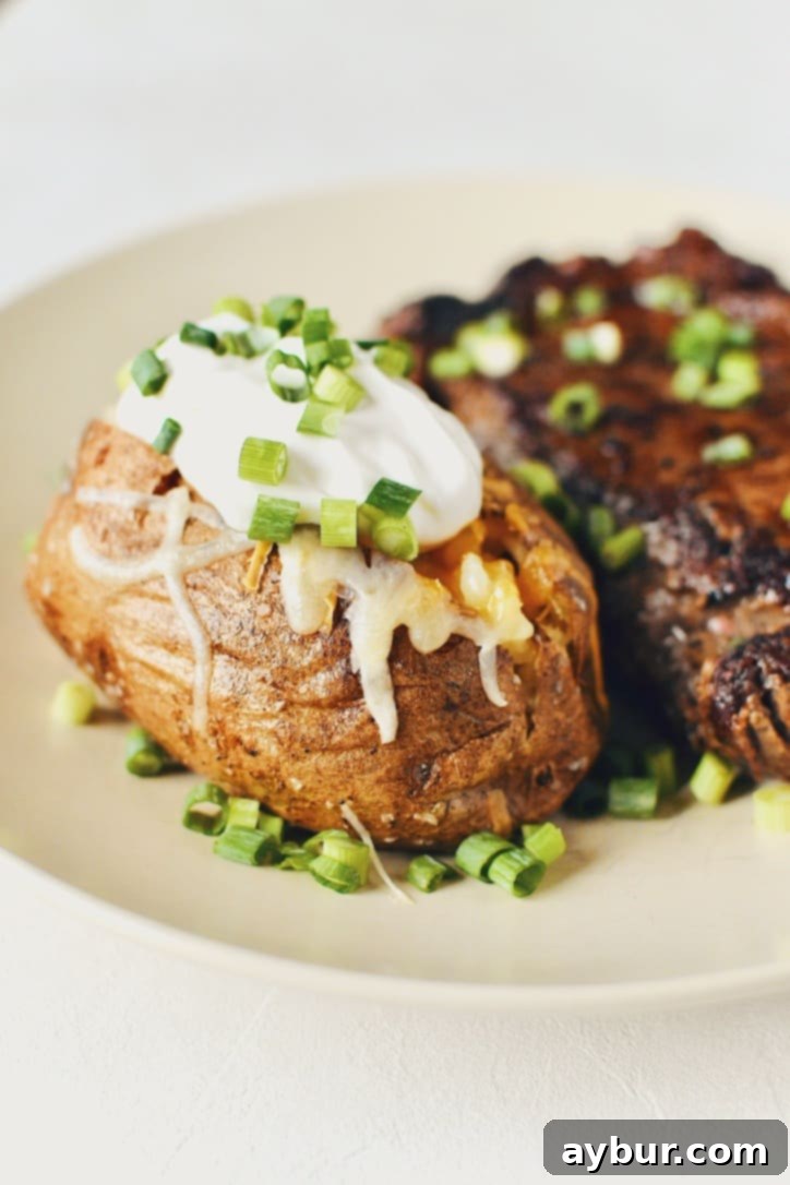 Crispy Skin Baked Potatoes elegantly topped with a generous layer of white and sharp cheddar cheeses, a dollop of sour cream, and a sprinkle of vibrant green onions.