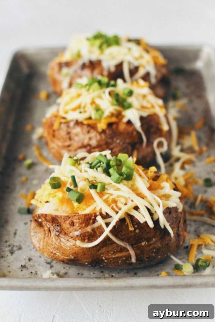 Crispy Skin Baked Potatoes topped with rich white and sharp cheddar cheeses and fresh green onions, ready for serving.