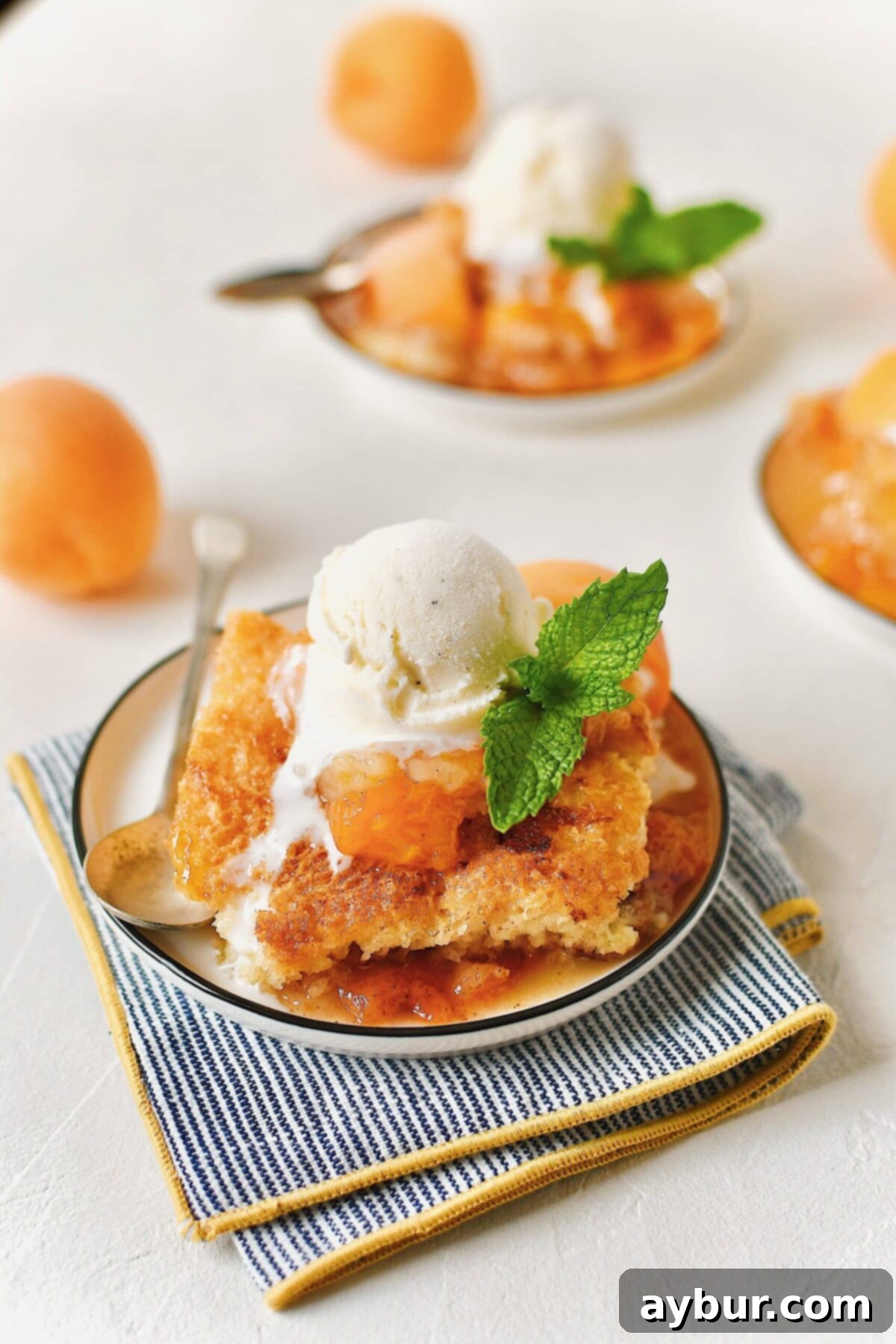 Golden Apricot Cobbler 12 A close-up of a delightful Apricot Cobbler served in a small bowl, garnished with a sprig of mint and a fresh apricot slice, alongside a spoon and a melting scoop of vanilla ice cream.