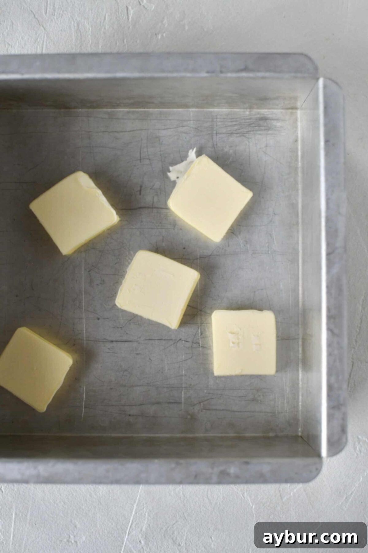 Golden Apricot Cobbler 5 Solid block of butter placed at the bottom of a shiny 8x8 metal baking tin.