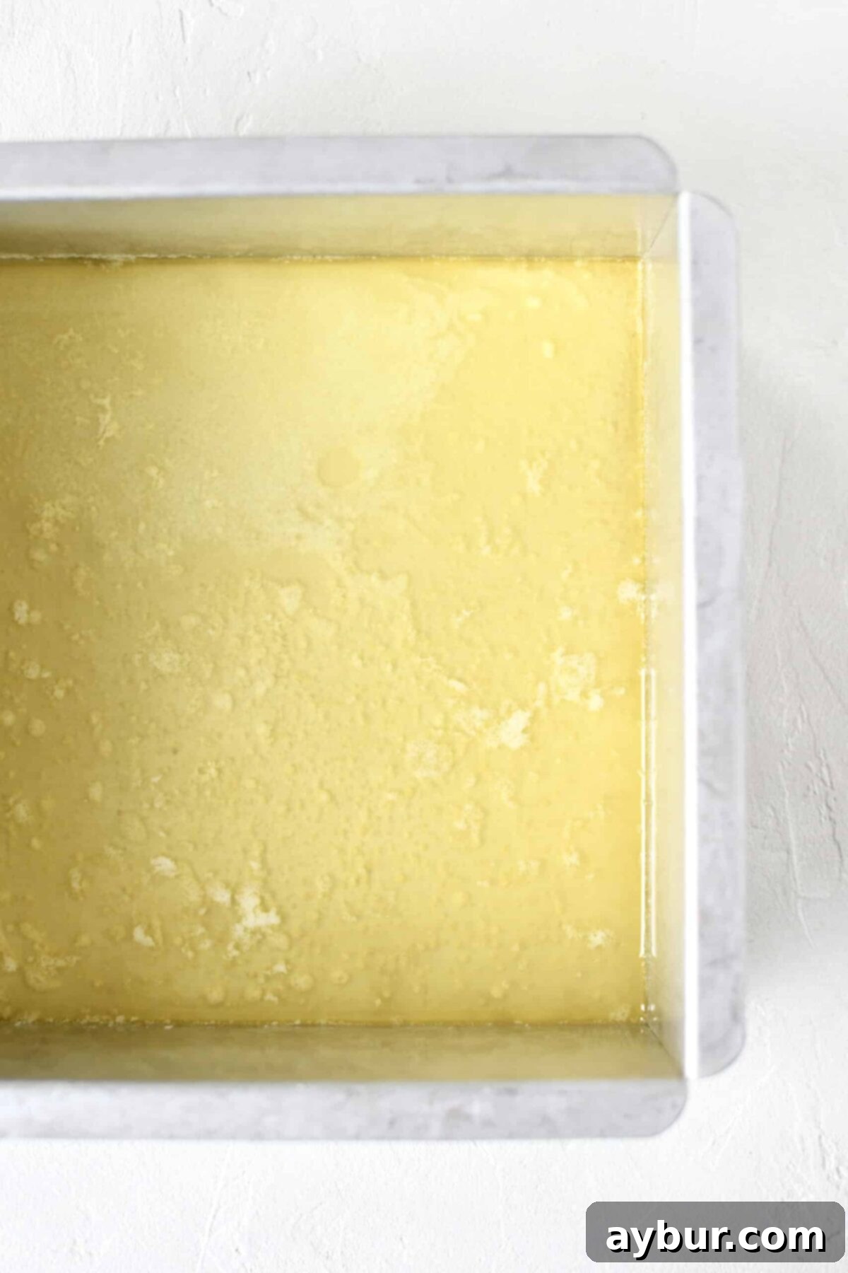 Golden Apricot Cobbler 6 Golden melted butter pooled evenly at the bottom of an 8x8 metal baking tin, ready for the next layer.