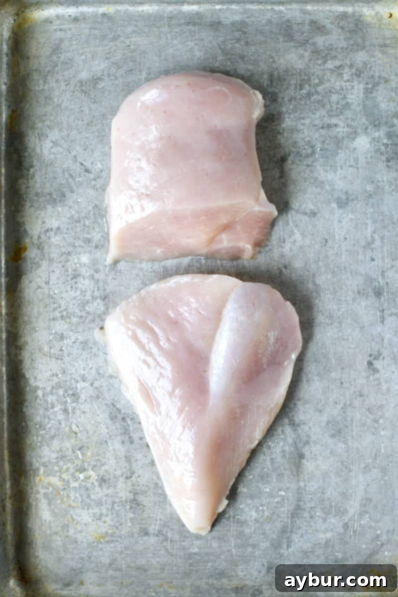 A raw chicken breast split in half, ready for tenderizing.