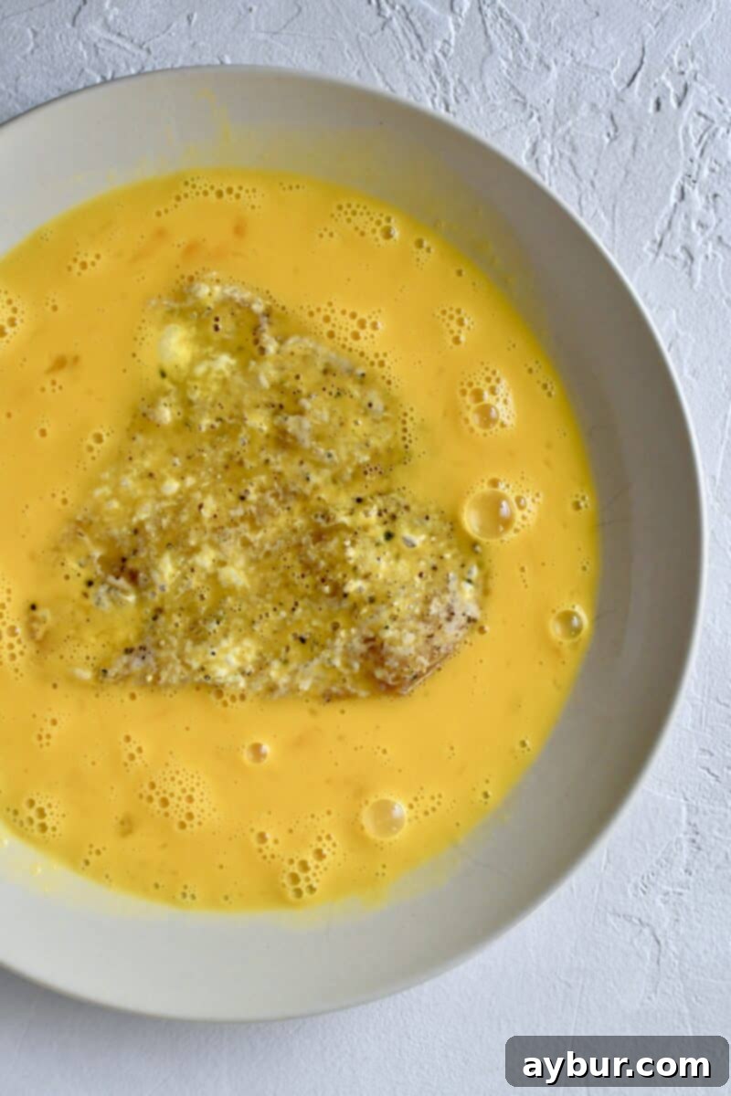 Chicken breast being dipped into beaten eggs as part of the dredging process.