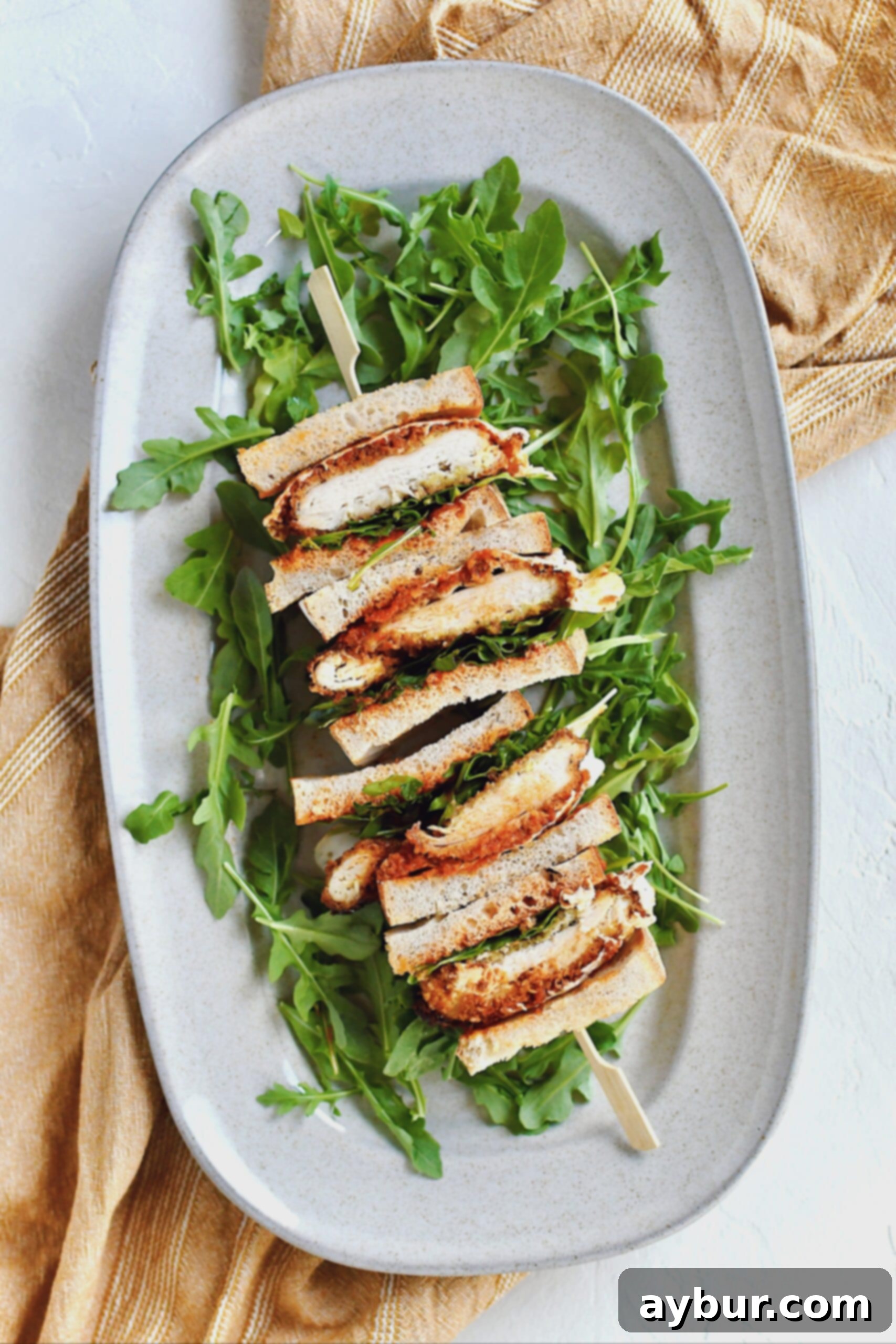 A perfectly sliced and stacked Crispy Parmesan Chicken Sandwich resting on a bed of fresh arugula, beautifully presented on a platter.