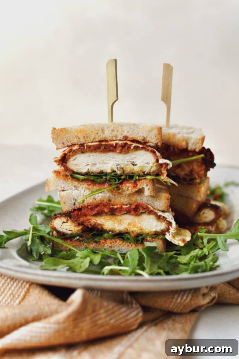 A beautifully presented Parmesan Chicken Sandwich, sliced in half and stacked artfully, resting on a bed of fresh arugula on a elegant platter.
