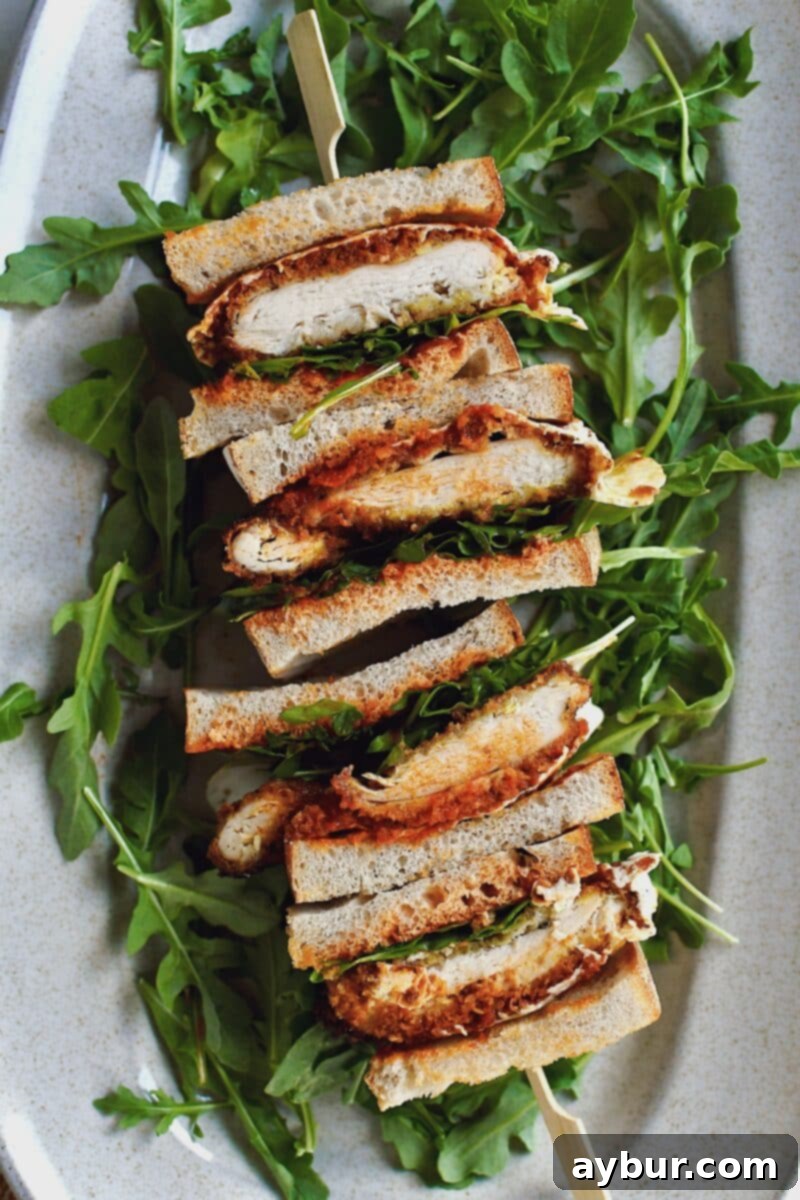 Another view of the Parmesan Chicken Sandwich, perfectly sliced and stacked, elegantly arranged on a platter with fresh arugula.