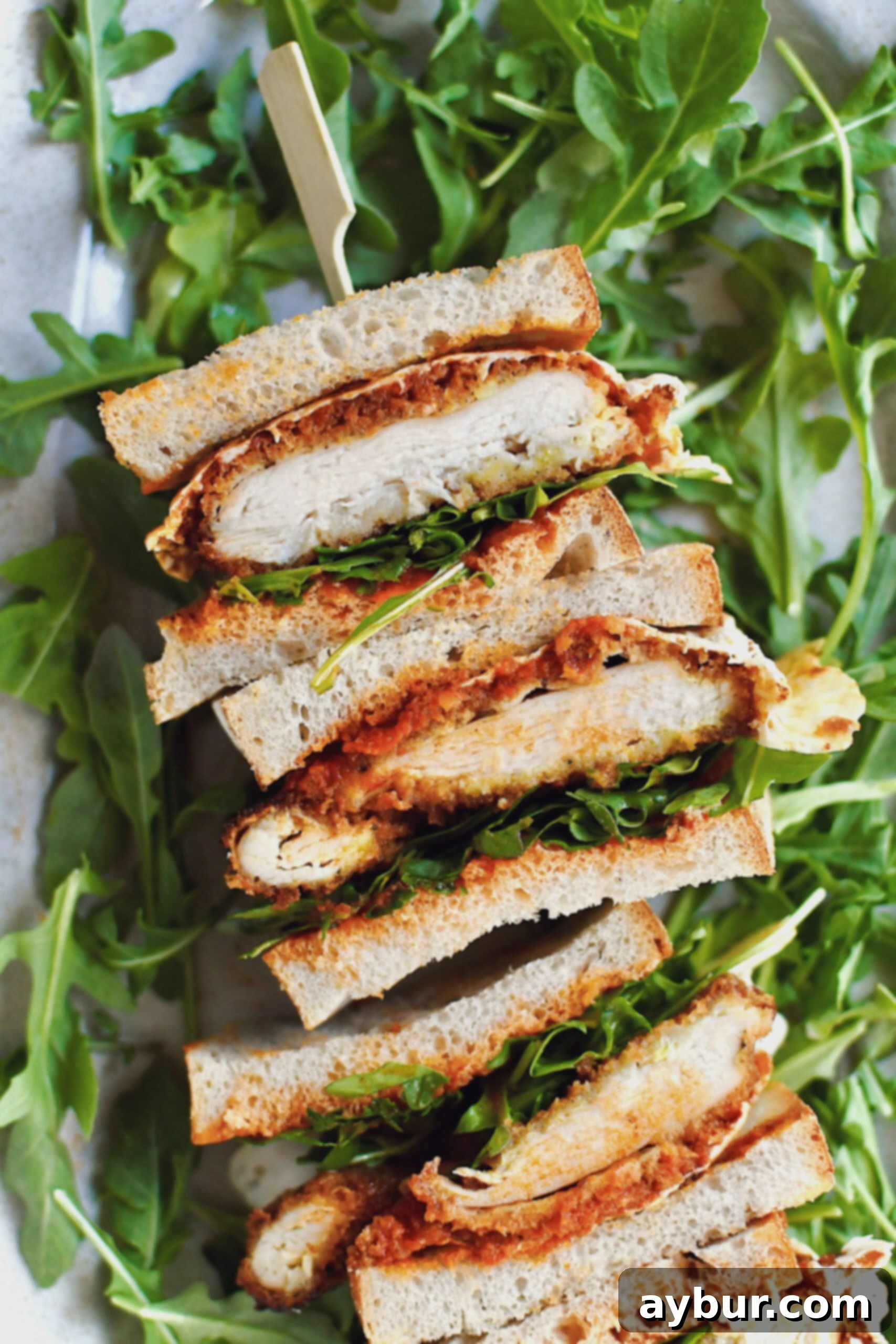 A stunning close-up of a Parmesan Chicken Sandwich, sliced and stacked high, beautifully arranged on a platter with a vibrant bed of fresh arugula.