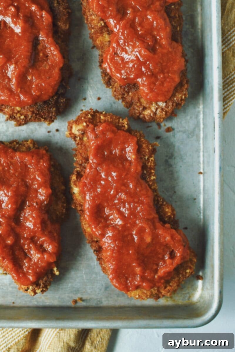 Crispy Parmesan Chicken cutlet topped with a generous layer of vibrant marinara sauce, preparing for the next step.