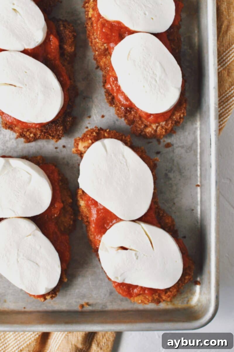 Crispy Parmesan Chicken with marinara sauce, now adorned with slices of fresh mozzarella cheese, awaiting melting.