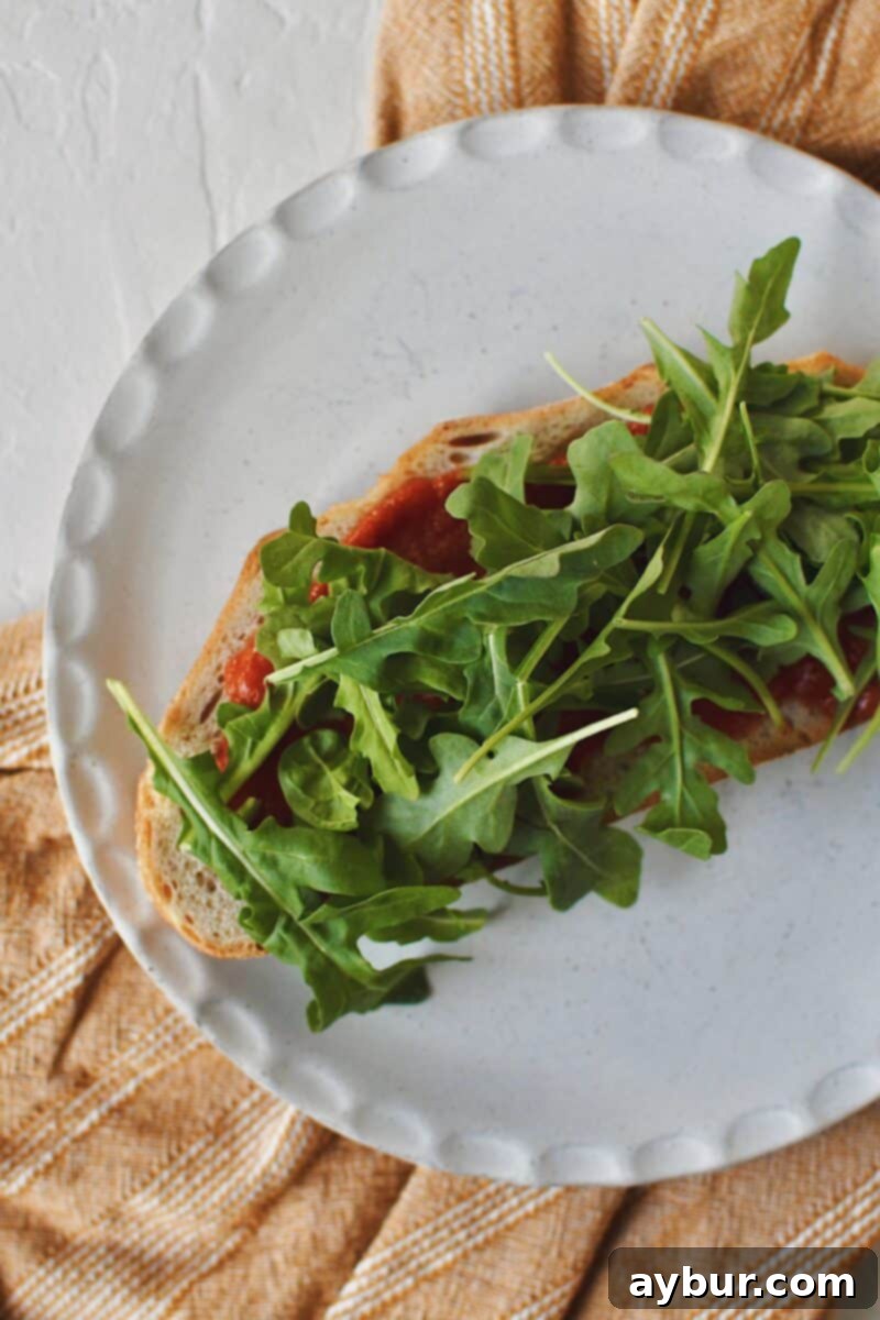 Toasted Italian bread with marinara, now topped with a generous layer of fresh, vibrant arugula, adding a peppery crunch.