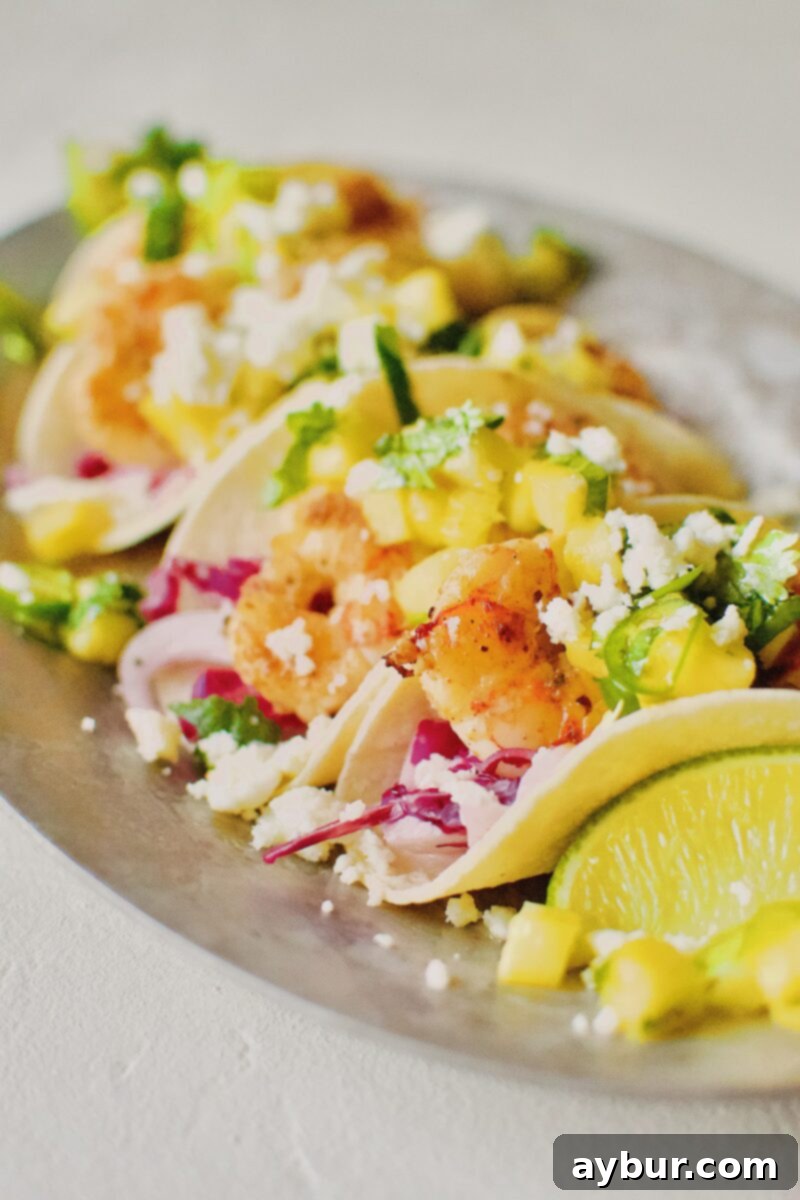 An assembled Baja Shrimp Taco held in hand, showcasing the layers of slaw, shrimp, pico, and cheese, ready to be enjoyed.