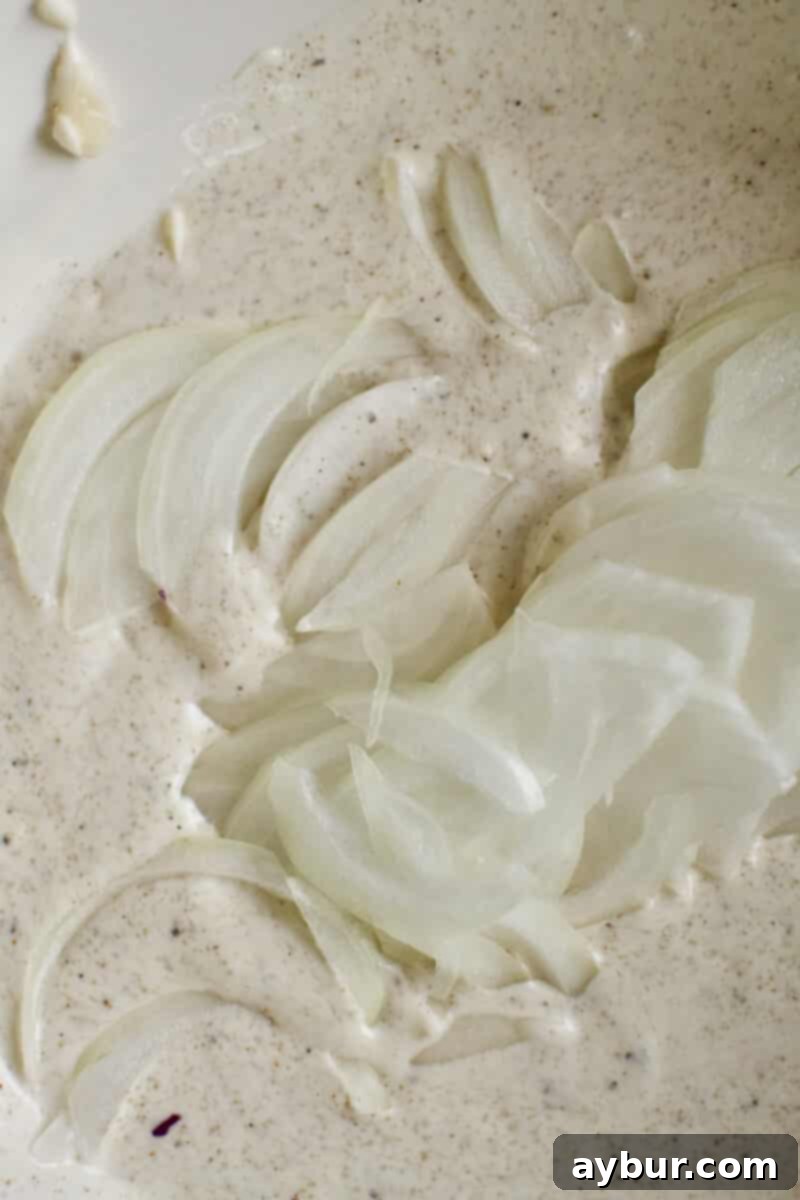 Thinly sliced onions being carefully added to the prepared dressing for the red cabbage slaw, allowing them to mellow.