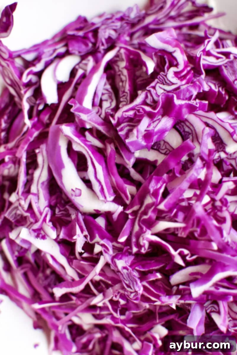 A mound of vibrant, finely shredded red cabbage, showcasing its beautiful purple hue, ready to be added to the slaw.
