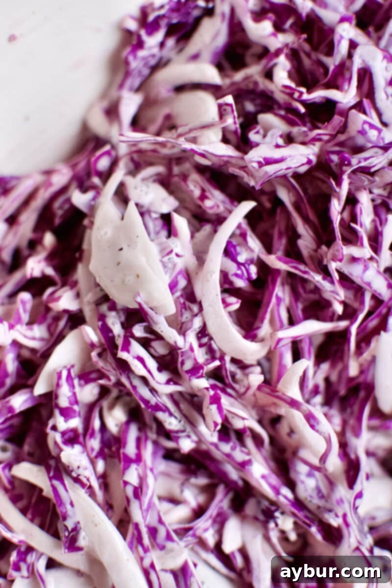 The red cabbage being mixed into the dressing and onions for the slaw, ensuring every strand is coated for optimal flavor.
