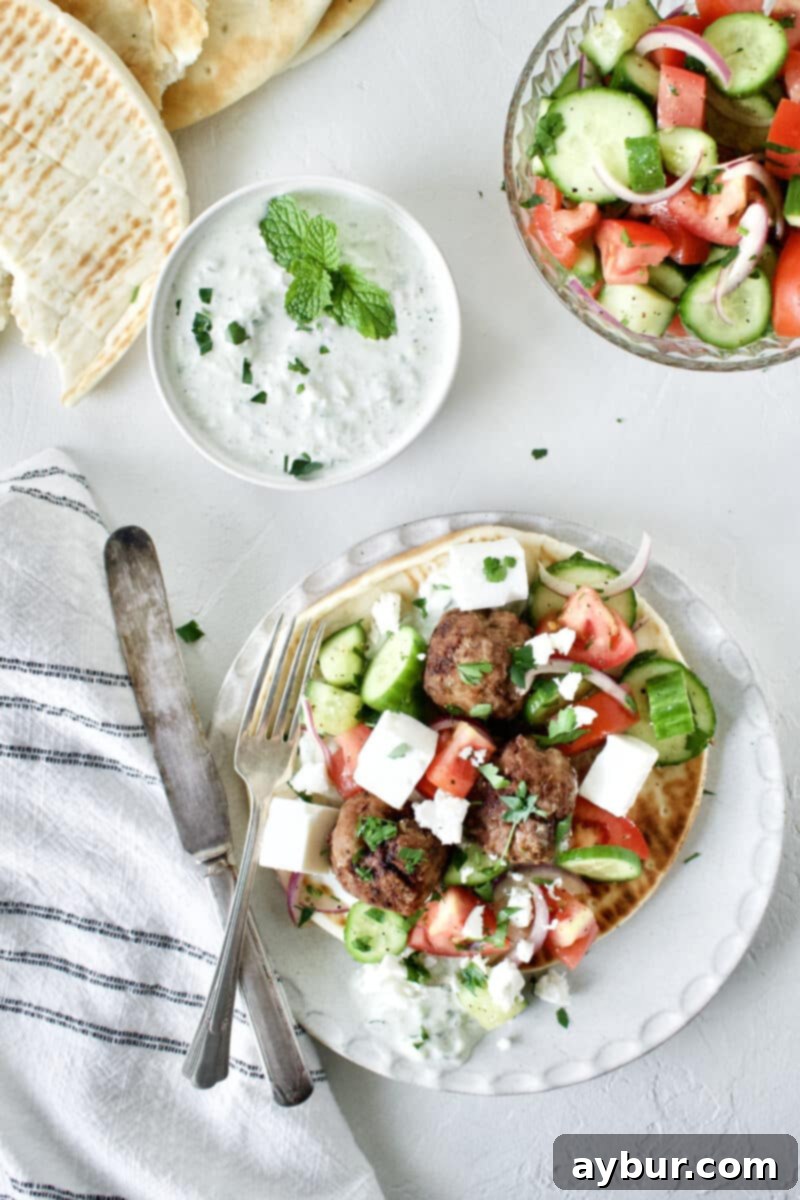 A generous serving of Greek Meatballs, vibrant Greek Salad, and creamy Tzatziki on pita bread, photographed from a close-up, appealing angle.