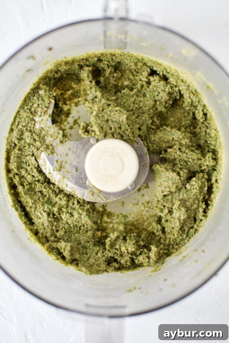Fresh Basil Pesto, in the bottom of a food processor, after adding olive oil, showing a rich green texture.
