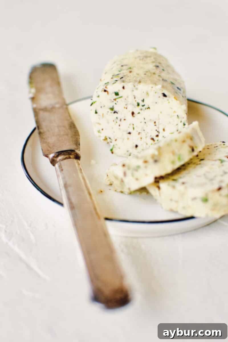 Gourmet Black Truffle Butter 14 A beautifully presented log of Black Truffle Butter on a white serving plate, with a knife poised to slice, highlighting its readiness for a gourmet meal.