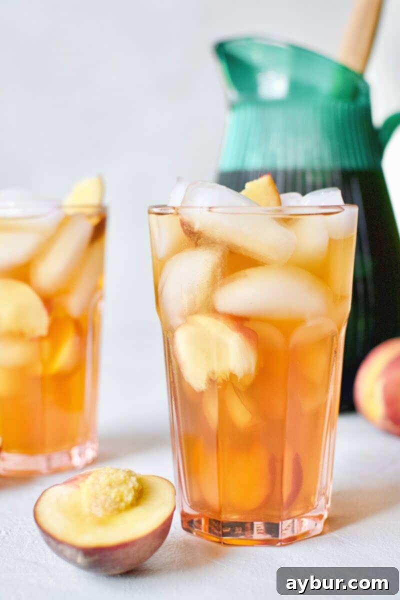 A chilled glass of vibrant Peach Sangria, garnished with fresh peach wedges and ice, ready to be enjoyed on a warm day.