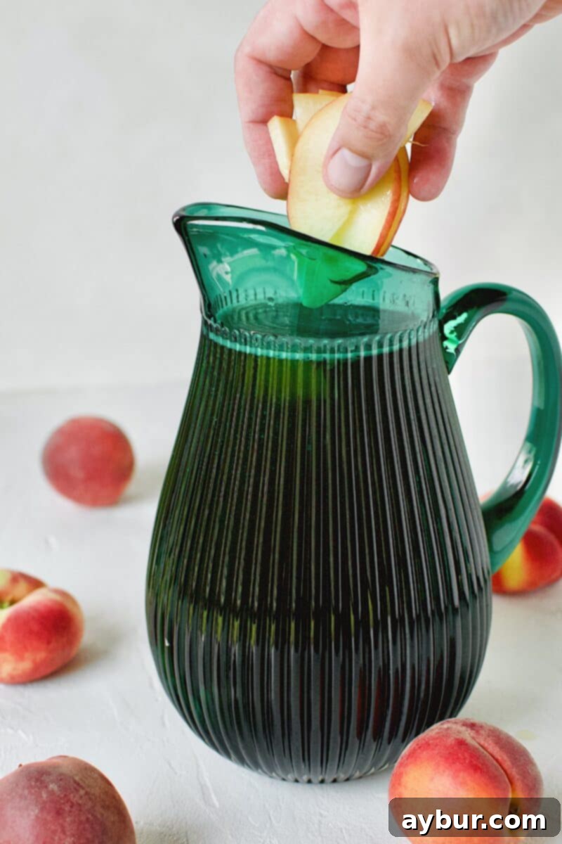 Freshly sliced peaches being gently dropped into a pitcher, joining the wine and sweet tea mixture to create sangria.