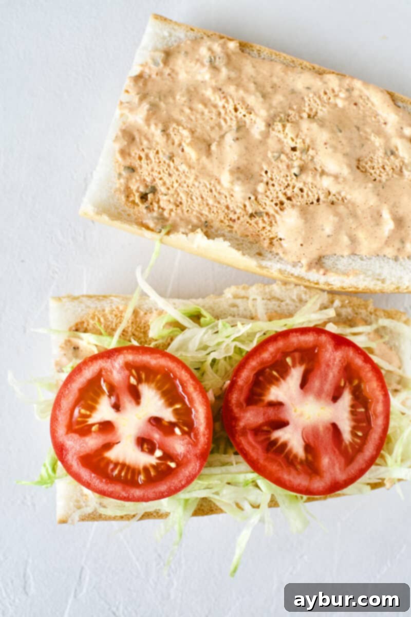 Building a Shrimp Po'boy Sandwich: French bread with remoulade, shredded lettuce, and juicy tomato slices layered on top.