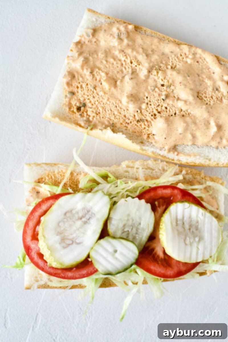 Building a Shrimp Po'boy Sandwich: French bread with remoulade, lettuce, tomatoes, and tangy dill pickle slices for added flavor.