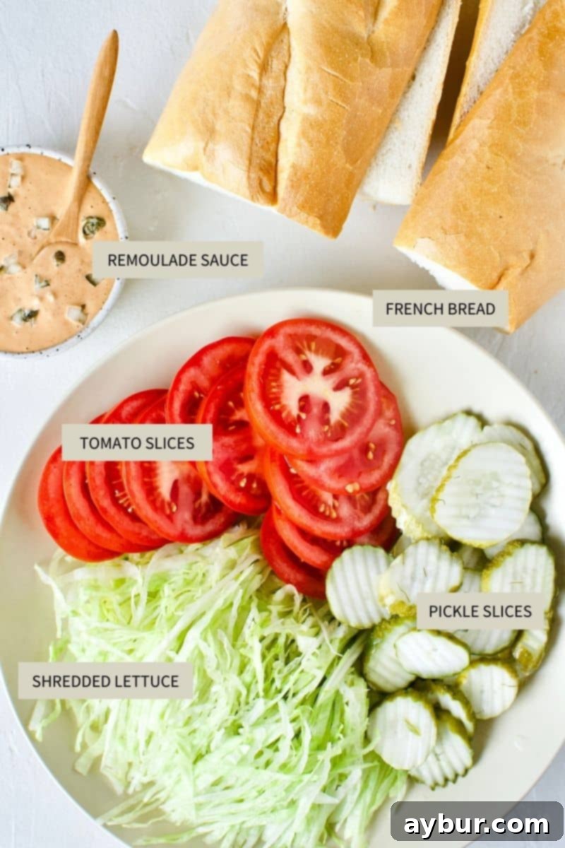Prepared French bread, homemade remoulade sauce, crisp iceberg lettuce, sliced tomatoes, and dill pickles, all ready for Po'boy sandwich assembly.