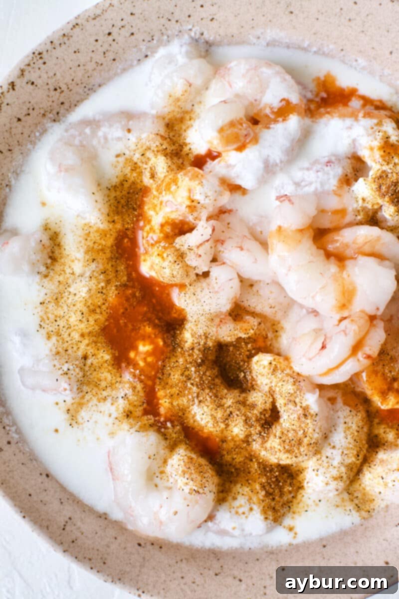 Shrimp marinating in a mixture of buttermilk, hot sauce, and creole seasoning, preparing for frying.